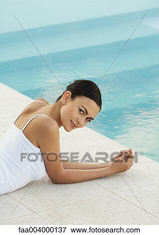 Stock Photo - Woman lying on ground near pool, looking over shoulder at camera. Fotosearch