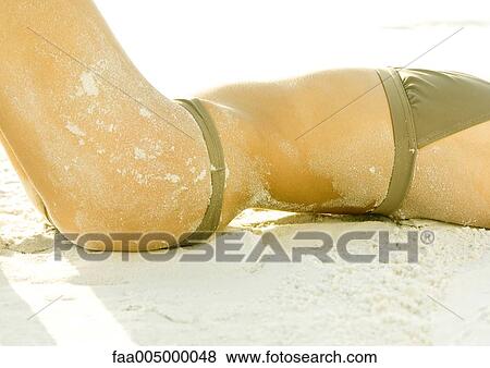 Stock Photo - Woman lying on sand, mid-section. Fotosearch