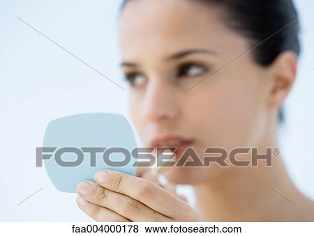 Woman putting on lipstick, focus on hand holding mirror in foreground View Large Photo Image Stock Photo - Woman putting on lipstick, focus on hand holding mirror in foreground. Fotosearch