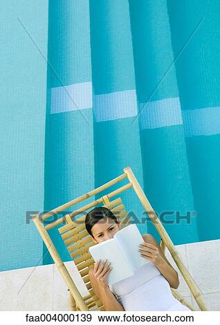 Stock Photo - Woman reading in lounge chair next to pool. Fotosearch
