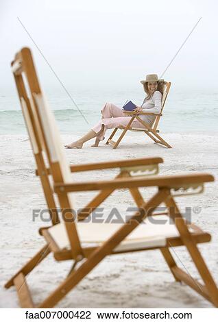 Woman sitting in beach chair, empty chair in foreground View Large Photo Image Stock Image - Woman sitting in beach chair, empty chair in foreground. Fotosearch