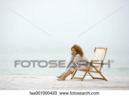 Stock Image - Woman sitting in beach chair, stretching. Fotosearch