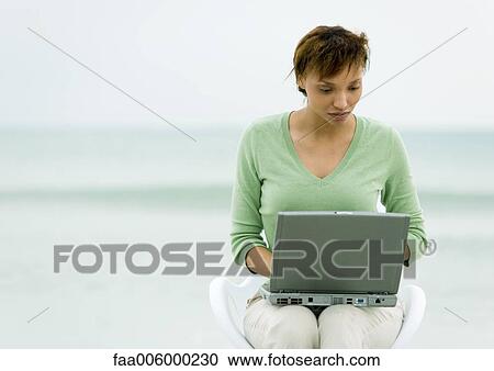 Woman sitting in chair using laptop, sea in background View Large Photo Image Stock Image - Woman sitting in chair using laptop, sea in background. Fotosearch