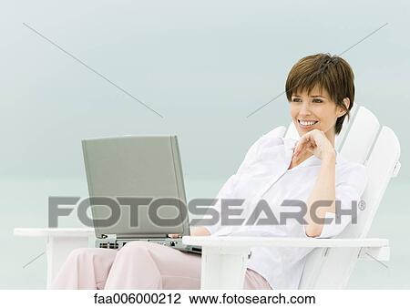 Woman sitting in deckchair using laptop, sea in background View Large Photo Image Stock Image - Woman sitting in deckchair using laptop, sea in background. Fotosearch