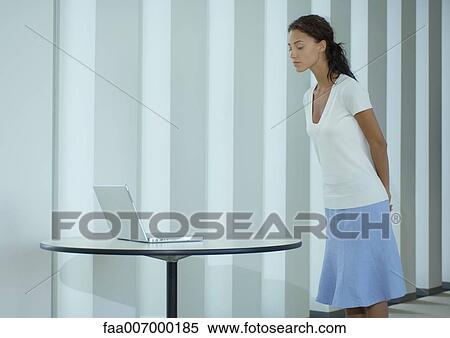 Woman standing, looking at laptop on table View Large Photo Image Stock Photography - Woman standing, looking at laptop on table. Fotosearch