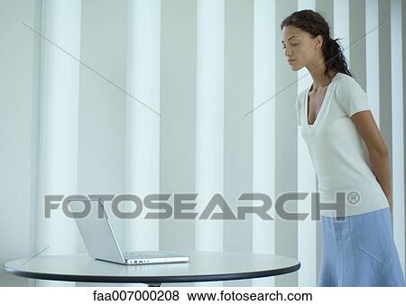 Stock Photo - Woman standing, looking down at laptop. Fotosearch