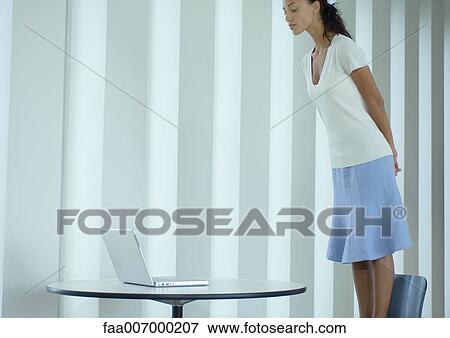 Stock Photo - Woman standing on chair, looking down at laptop. Fotosearch