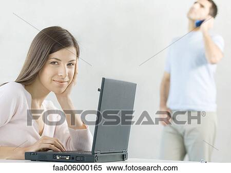 Stock Photography - Woman using laptop while husband uses cell phone in background. Fotosearch