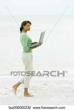 Woman walking on beach, carrying open laptop View Large Photo Image Stock Image - Woman walking on beach, carrying open laptop. Fotosearch