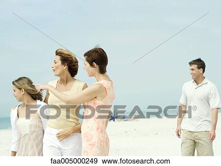 Stock Photo - Woman with friend and teenage girl on beach, pointing toward distance. Fotosearch