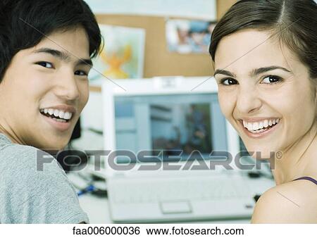 Young couple smiling, laptop in background View Large Photo Image Stock Photograph - Young couple smiling, laptop in background. Fotosearch