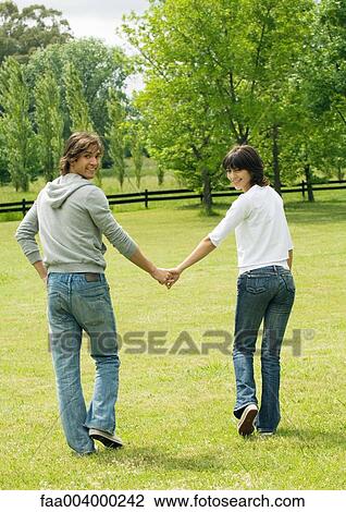 Young couple walking in field, smiling over shoulders at camera View Large Photo Image Stock Image - Young couple walking in field, smiling over shoulders at camera. Fotosearch