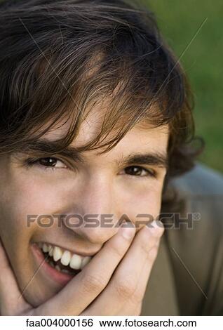 Stock Photograph - Young man laughing with hand over mouth, close-up. Fotosearch
