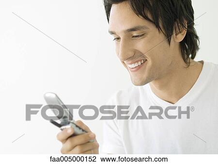 Young man looking at cell phone, smiling View Large Photo Image Stock Image - Young man looking at cell phone, smiling. Fotosearch