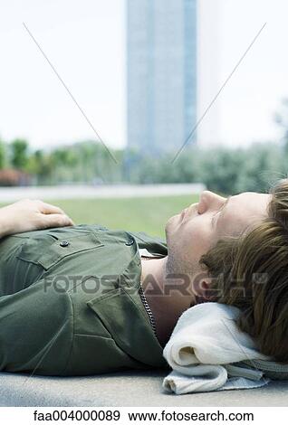 Stock Photo - Young man napping in city park, close-up. Fotosearch