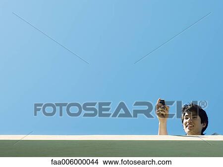 Young man using cell phone, low angle view with sky in background View Large Photo Image Picture - Young man using cell phone, low angle view with sky in background. Fotosearch