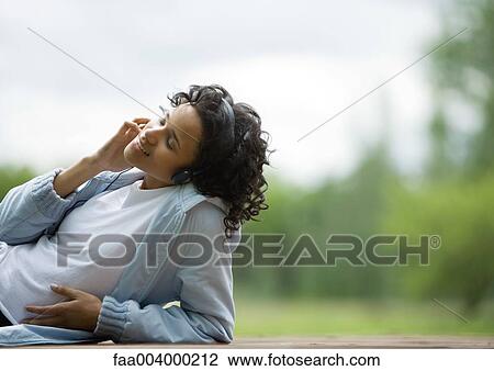 Young woman listening to headphones outdoors and smiling View Large Photo Image Stock Image - Young woman listening to headphones outdoors and smiling. Fotosearch
