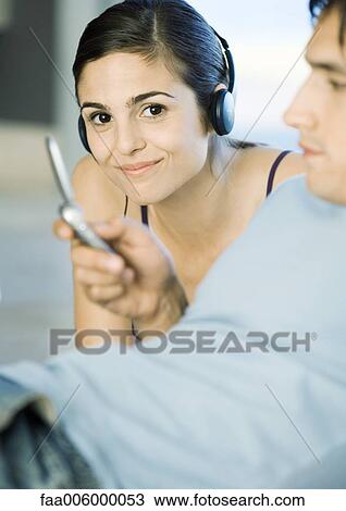 Young woman listening to headphones while male friends looks at cell phone View Large Photo Image Stock Image - Young woman listening to headphones while male friends looks at cell phone. Fotosearch