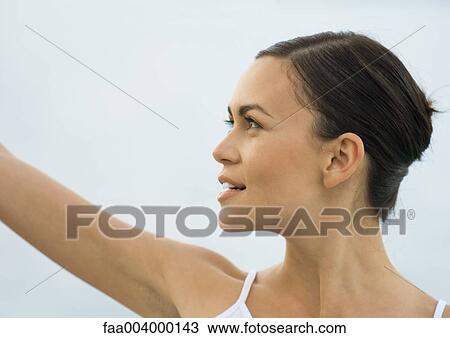 Stock Image - Young woman raising arm, side view. Fotosearch