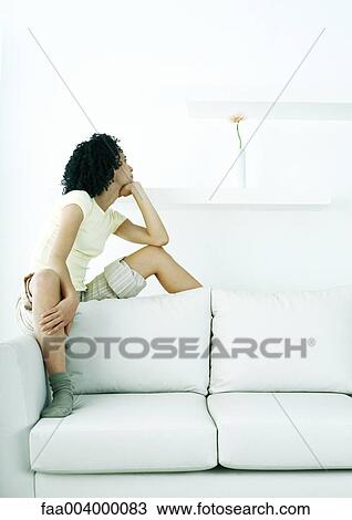 Young woman sitting on back of sofa, looking at flower in vase View Large Photo Image Stock Image - Young woman sitting on back of sofa, looking at flower in vase. Fotosearch
