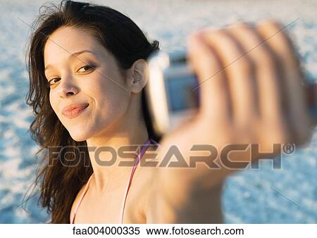 Stock Photography - Young woman taking photo of self on beach. Fotosearch