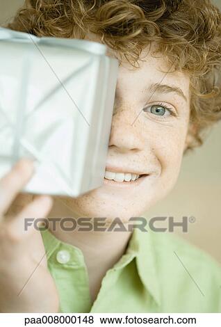 Boy holding up present in front of face View Large Photo Image Stock Photo - Boy holding up present in front of face. Fotosearch