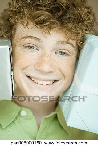 Stock Image - Boy holding up presents on either side of face. Fotosearch