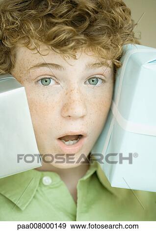 Stock Photo - Boy holding up presents on either side of face. Fotosearch