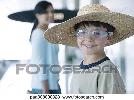 Stock Photo - Boy wearing goggles and straw hat in airport, smiling at camera. Fotosearch