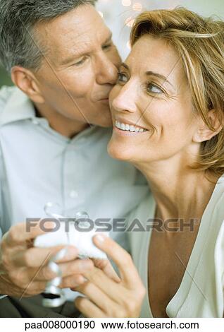 Stock Image - Couple exchanging christmas gift, man kissing woman on cheek. Fotosearch