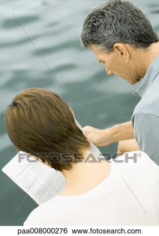 Couple reading newspaper together, water in background View Large Photo Image Stock Photograph - Couple reading newspaper together, water in background. Fotosearch