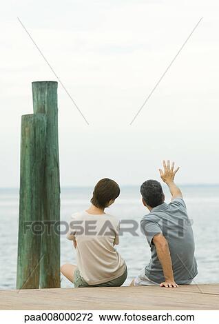 Couple sitting on edge of dock, man waving View Large Photo Image Stock Image - Couple sitting on edge of dock, man waving. Fotosearch