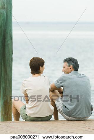 Couple sitting on edge of dock, waving View Large Photo Image Stock Image - Couple sitting on edge of dock, waving. Fotosearch