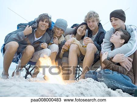 Group of friends sitting around campfire View Large Photo Image Stock Image - Group of friends sitting around campfire. Fotosearch
