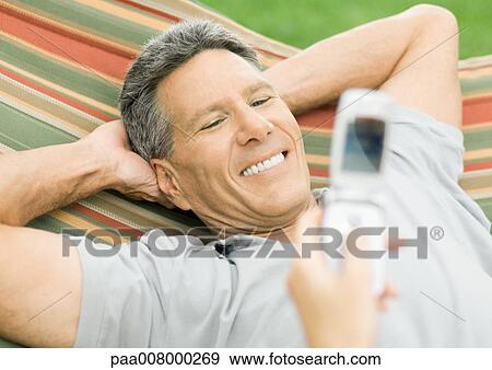 Stock Photo - Man in hammock smiling for photo being taken with cell phone. Fotosearch