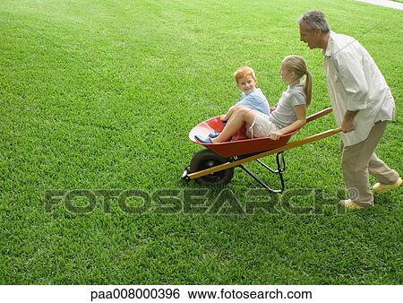 Man pushing two children in wheelbarrow View Large Photo Image Stock Photograph - Man pushing two children in wheelbarrow. Fotosearch