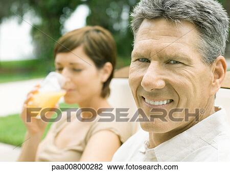 Stock Image - Man smiling as woman drinks juice in background. Fotosearch