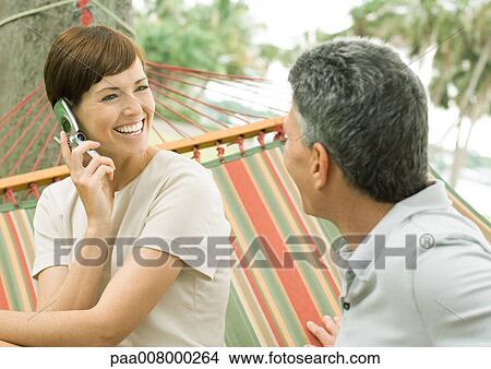 Mature couple lounging in hammock, woman using cell phone View Large Photo Image Picture - Mature couple lounging in hammock, woman using cell phone. Fotosearch