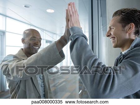 Two men holding up hands on either side of glass in airport, laughing View Large Photo Image Stock Photography - Two men holding up hands on either side of glass in airport, laughing. Fotosearch