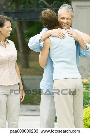 Woman hugging man as second woman watches smiling View Large Photo Image Stock Image - Woman hugging man as second woman watches smiling. Fotosearch