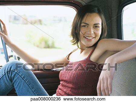 Stock Photograph - Young woman sitting inside vehicle, smiling at camera. Fotosearch