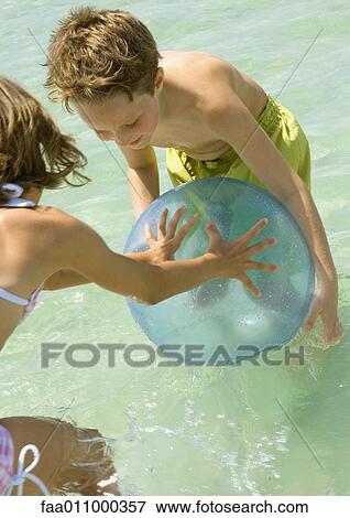 Stock Photo - Boy and girl playing with ball in sea. Fotosearch