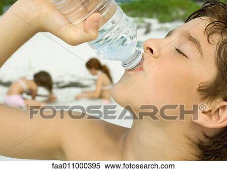 Boy drinking bottled water, girls playing in sand in background View Large Photo Image Stock Photography - Boy drinking bottled water, girls playing in sand in background. Fotosearch