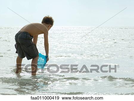Stock Photo - Boy filling bucket with water in surf. Fotosearch