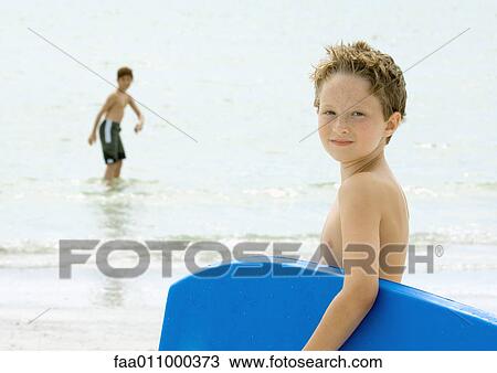 Boy holding body board, looking over shoulder at camera View Large Photo Image Stock Image - Boy holding body board, looking over shoulder at camera. Fotosearch