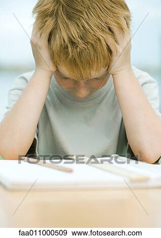 Stock Photo - Boy holding head and looking down at homework. Fotosearch