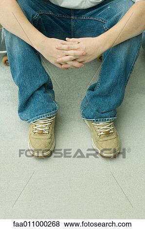 Boy sitting on skateboard with hands clasped, high angle view, low section View Large Photo Image Stock Photo - Boy sitting on skateboard with hands clasped, high angle view, low section. Fotosearch