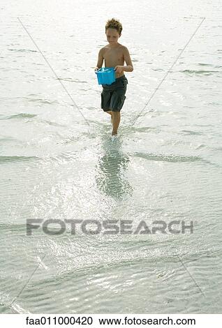Boy walking through surf with bucket full of water View Large Photo Image Stock Image - Boy walking through surf with bucket full of water. Fotosearch