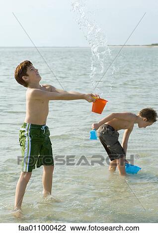 Stock Image - Boys playing in ocean with buckets. Fotosearch