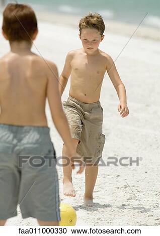 Stock Image - Boys playing with soccer ball on beach. Fotosearch